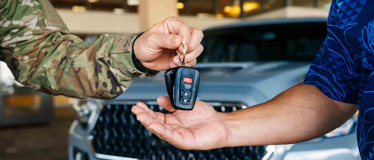 The military person gives the sales representative their car keys after selling their car.
