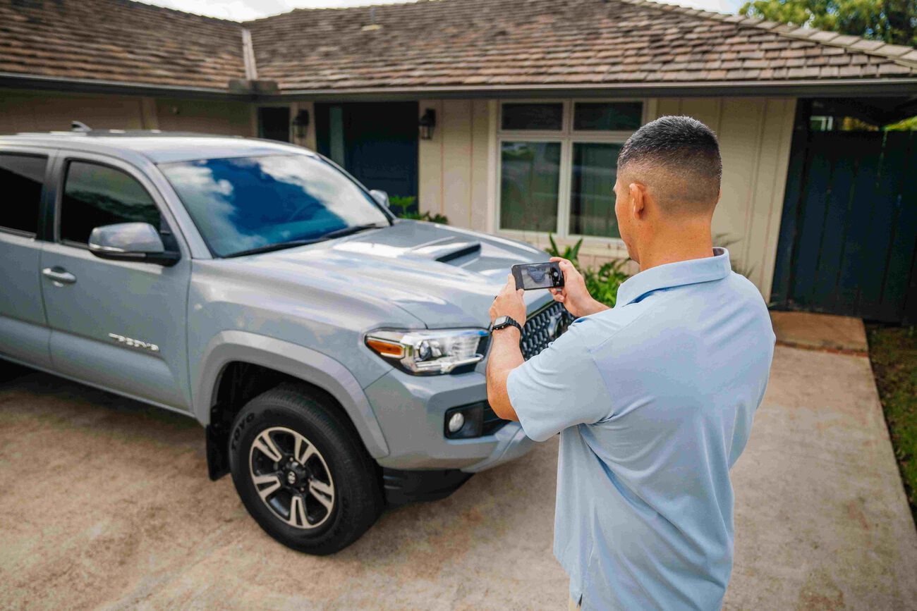 The man is taking a picture of his truck to send to the Servco Buying Center for review.